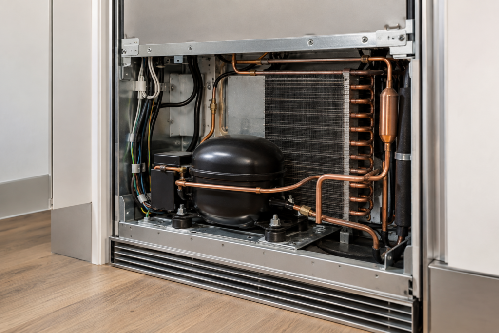 The rear service niche of a built-in wine column with its back panel removed, showing copper tubing and the compressor.